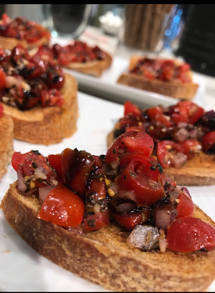 Slices of toasted bread topped with chopped tomatoes, onions, herbs, and balsamic glaze on a white plate.