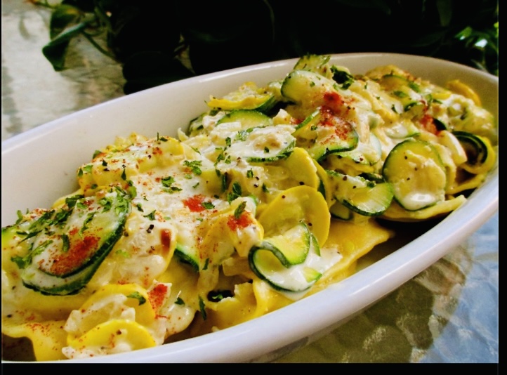 Oval dish filled with ravioli, creamy sauce, zucchini slices, and herbs, garnished with paprika and black pepper.