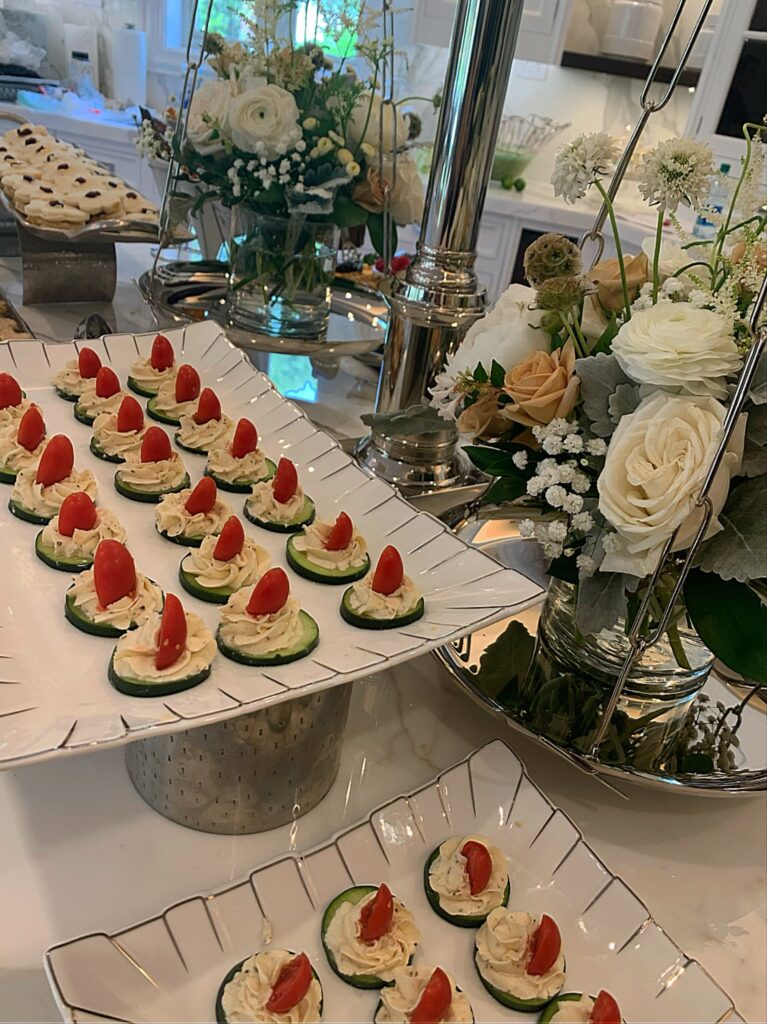 Plates of cucumber slices topped with cream and tomato are arranged on a countertop with floral centerpieces nearby.