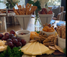 Charcuterie board with assorted cheeses, crackers, grapes, dried fruit, breadsticks, and nuts on a wooden table.