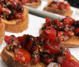 Slices of toasted bread topped with chopped tomatoes, onions, herbs, and balsamic glaze on a white plate.