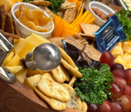 A wooden tray with assorted cheeses, crackers, fruit, dried fruit, and garnish, arranged for serving.
