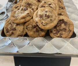 A tray of chocolate chip cookies arranged in rows with a small chalkboard sign labeled "Chocolate Chip Cookies.