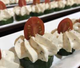 Rows of cucumber slices topped with piped cream cheese and half of a cherry tomato, arranged on a white platter.
