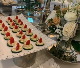 Plates of cucumber slices topped with cream and tomato are arranged on a countertop with floral centerpieces nearby.