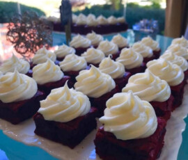 Rows of red velvet cake squares topped with swirls of white frosting on a rectangular platter.
