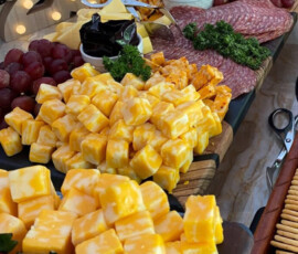 Charcuterie board with cubed cheese, sliced meats, grapes, strawberries, almonds, and a lit "2023" sign in the background.