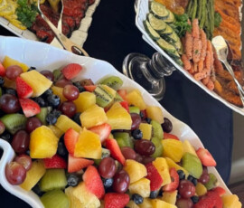 Platters of fresh fruit salad, grilled vegetables, and assorted appetizers arranged on a table for a buffet.