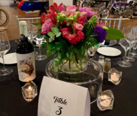 Table with a flower centerpiece, wine, and candles, set in a gallery with motorcycles and art on display in the background.