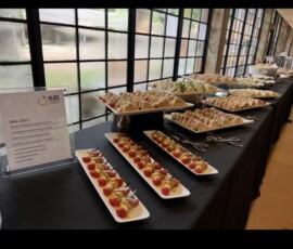 A buffet table with assorted sandwiches and appetizers on trays, set near large windows with natural light.