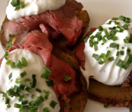 Three potato slices topped with roast beef, sour cream, and chopped chives on a plate.