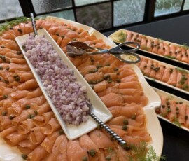 Plates of sliced smoked salmon garnished with capers and dill, served with chopped red onions and utensils.
