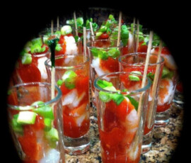 Shrimp cocktail shooters in shot glasses, garnished with chopped green onions, arranged on a granite countertop.