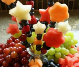 Fruit arrangement with grapes, cantaloupe, and star-shaped and flower-shaped melon skewers in a glass vase.