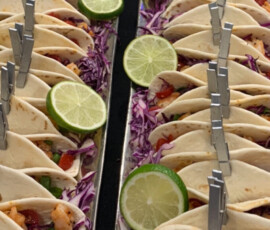 Rows of mini tacos filled with vegetables, garnished with lime slices and held upright by small clothespins.