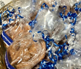 A basket filled with clear bags of chocolate turtles tied with blue and white ribbons, arranged for display.