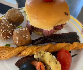Plate with a small sandwich, meatballs, breadstick, grilled meat, cheese, black olive, tomato, and pepperoni skewer.