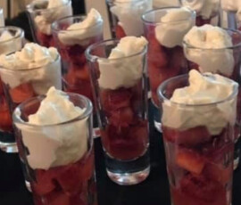 Small glasses filled with diced strawberries and topped with whipped cream are arranged on a black surface.